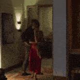 a man in a black shirt and a woman in a red dress are standing in a hallway .
