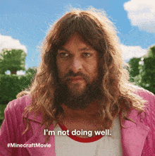a man with long hair and a beard says " i 'm not doing well " while wearing a pink jacket
