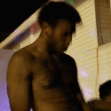 a shirtless man with a tattoo on his chest is standing in front of a building at night .