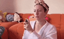 a woman wearing a headband is spraying something on her face while sitting on an orange couch