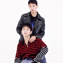 two young men standing next to each other with one wearing a leather jacket