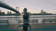 a woman is dancing on a pier in front of a bridge