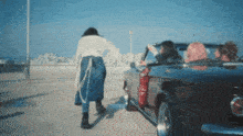 a woman is walking towards a convertible car