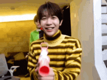 a young man wearing a yellow and brown striped sweater is holding a pink toy gun .