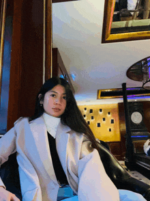 a woman in a white coat sits in a chair in front of a mirror
