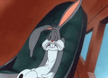 bugs bunny from looney tunes is sitting in a chair with his eyes closed .