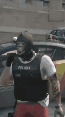 a man wearing a vest that says policia is standing in front of a police car