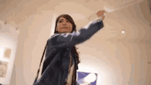 a woman in a blue jacket is standing in a room with her arms outstretched and looking up at the ceiling .