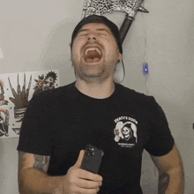 a man wearing a death 's door t-shirt laughs while holding a cell phone