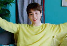 a young man wearing a yellow sweater is smiling with his arms outstretched