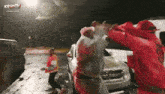 a man in a red jacket is standing in front of a white truck with the words nowthis tv on the bottom