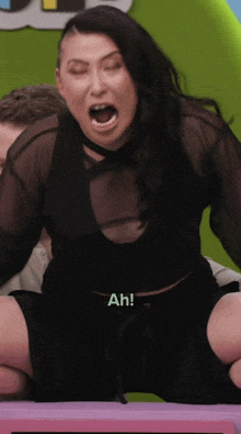 a woman in a black top and black shorts is sitting on a table with her mouth open and says ah