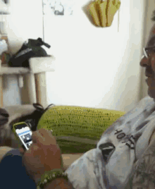 a man sitting on a couch holding a cell phone and wearing a shirt that says ' hawk ' on it