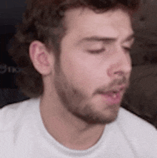 a close up of a man 's face with his eyes closed and a beard wearing a white shirt .