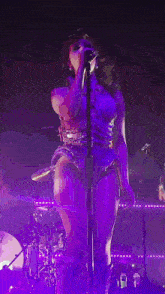 a woman is singing into a microphone on a stage in a purple light .