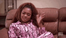 a woman is sitting on a couch wearing a pink snake print shirt and pajamas .