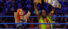 two women are standing in a wrestling ring holding up their arms .