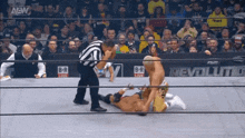 a wrestler is laying on the ground in a wrestling ring while a referee watches .