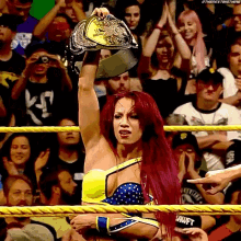 a woman in a wrestling ring holds up a championship belt in front of a crowd