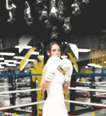 a woman in a white dress wearing boxing gloves stands in a boxing ring