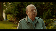 a man in a green jacket stands in a park