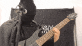 a man in a black cape is playing a guitar in front of a black flag that says snm