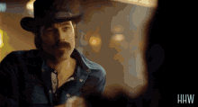 a man wearing a cowboy hat and a denim shirt has the letters hw on the bottom