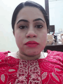 a woman wearing a red top with gold embroidery looks down at the camera