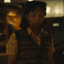a woman with blood on her face is wearing a sweater vest and a yellow shirt