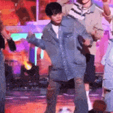 a man in a blue shirt is dancing on a stage with a microphone in his hand .