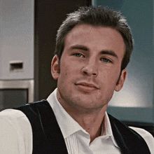 a man wearing a white shirt and a black vest looks at the camera