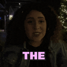 a woman with curly hair is standing in front of a sign that says " everything "