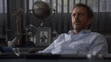 a man sits at a desk with his hands behind his head in front of a globe