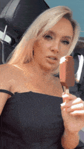 a blonde woman in a black dress is holding a chocolate ice cream bar