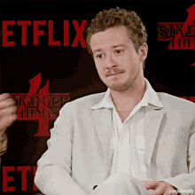 a man in a white suit is standing in front of a stranger things poster