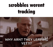 a man with glasses is holding a cell phone in his hand and asking why arnt they leaving yet ?