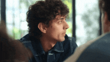 a man with curly hair is sitting at a table with other people and the name jayanne is on the bottom right