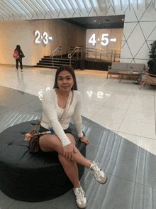 a woman sits on a ottoman in front of a sign that says 2-3 4-5