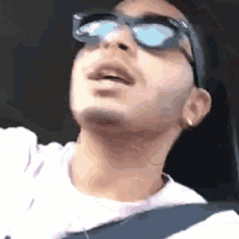 a man wearing sunglasses is driving a car and looking up .