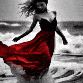 a black and white photo of a woman in a red dress dancing in the ocean .
