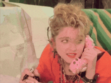 a woman is talking on a pink telephone