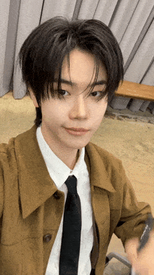 a young man wearing a brown jacket and black tie taking a selfie