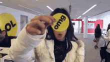 a woman holds up a yellow circle with the word omg on it