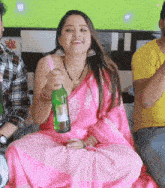 a woman in a pink saree is holding a green bottle of beer