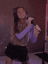 a woman singing into a microphone wearing headphones and a purple top