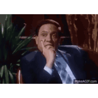a man in a suit and tie is sitting in a chair holding his hand to his chin .