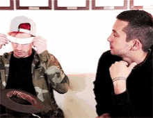 two men are sitting on a couch and one of them is putting a bandage on his face .