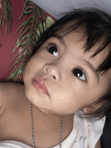 a baby girl with a necklace around her neck looks at the camera