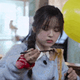 a young girl is eating noodles with chopsticks in front of a yellow balloon .