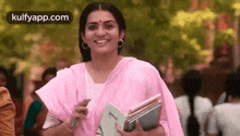 a woman in a pink sari is smiling while holding a book and a pen .